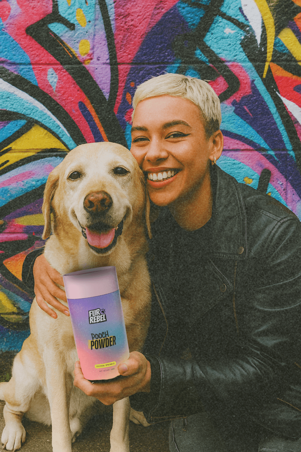 Person with a dog holding tube of fur rebel pooch powder dog supplement against a colorful graffiti wall.
